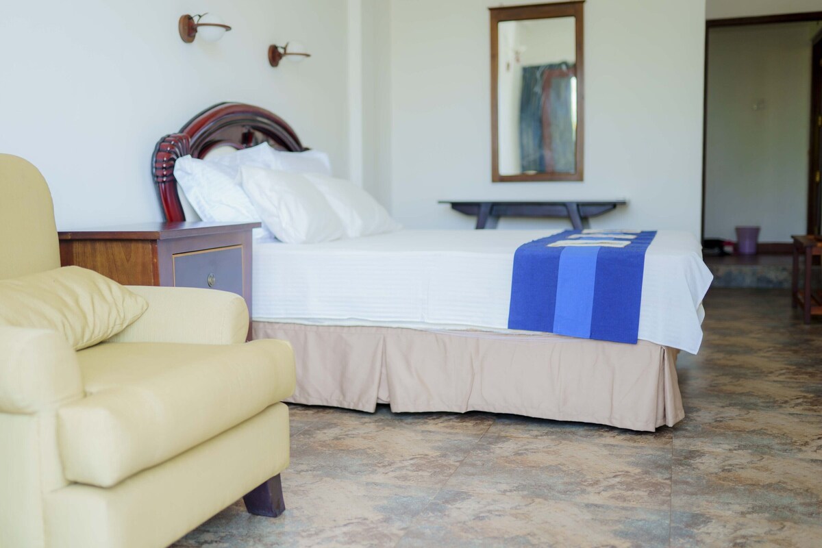 Una habitación de hotel con cama, una silla, una mesita de noche y un espejo.