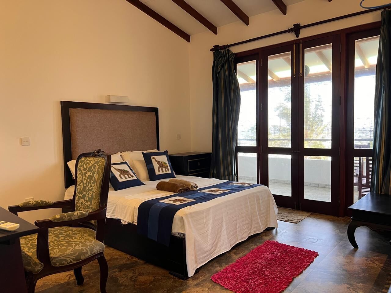 A bedroom with a bed, a chair, a desk, and a red rug.