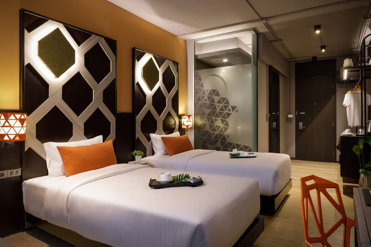 A hotel room with two beds, a wardrobe, a mirror, and a small table with a tray.