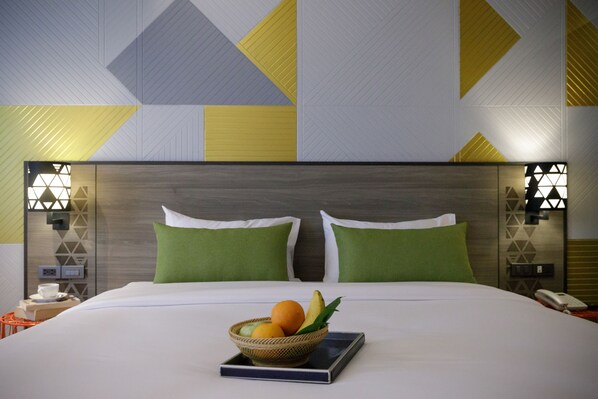 A hotel room with a large bed, green pillows, a bedside table with a phone, and a wall with geometric patterns.