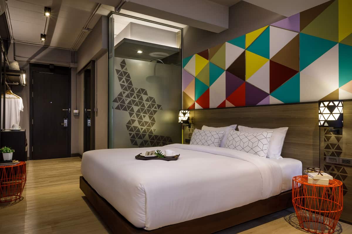 A modern hotel room with a large bed, a geometric wall mural, and a small table with a tray.