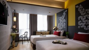 Habitación de hotel con dos camas, un escritorio, una silla, un televisor y una gran obra de arte geométrica en la pared.