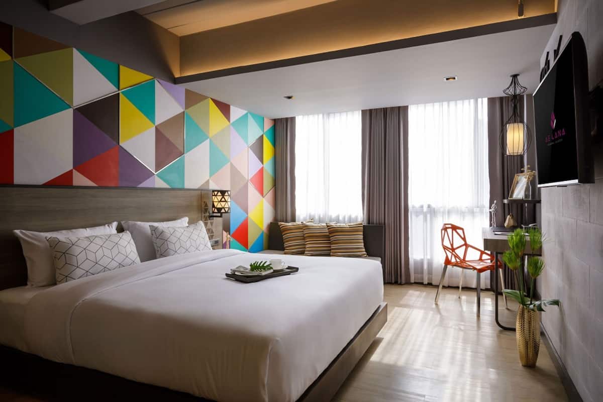 A modern hotel room with a large bed, a TV, a desk, and a chair.