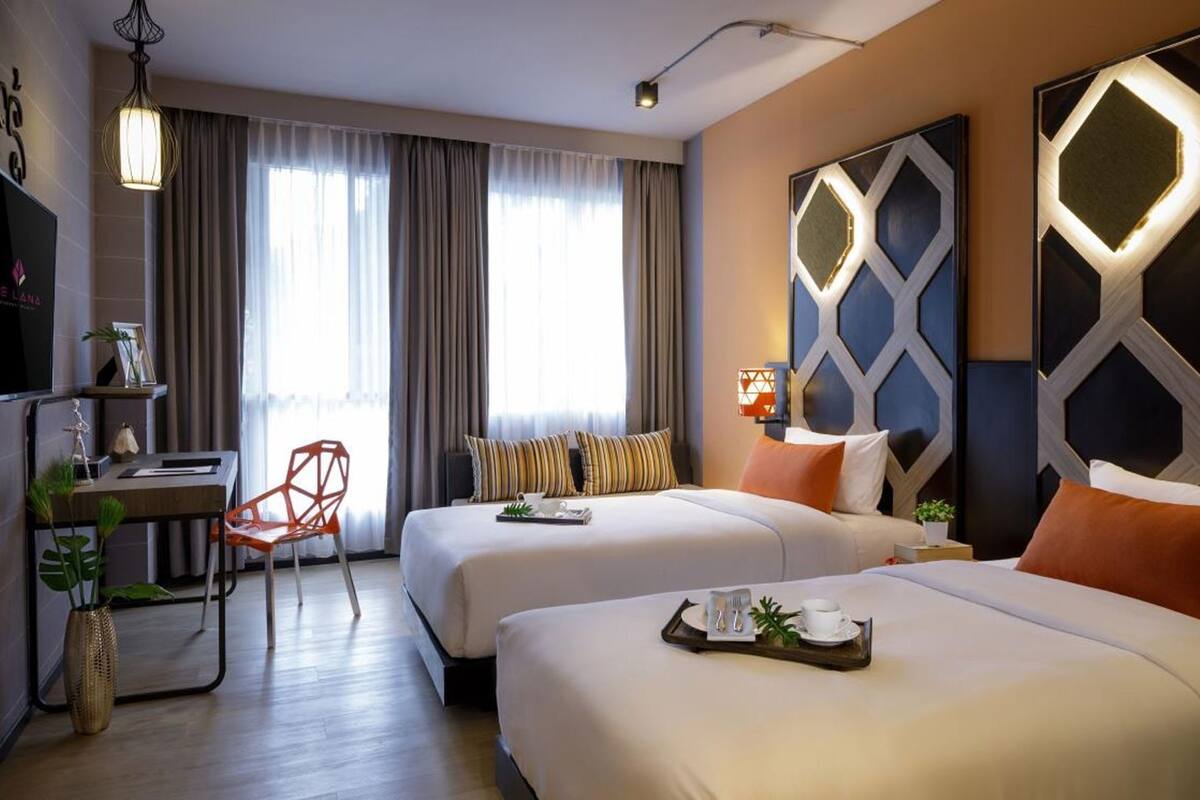 A hotel room with two beds, a desk, a chair, and a large geometric wall decoration.