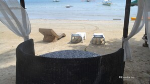 A beachside seating area with wicker chairs and tables, overlooking the sea with boats in the distance. - Floresita's Beach Resort (El Nido)