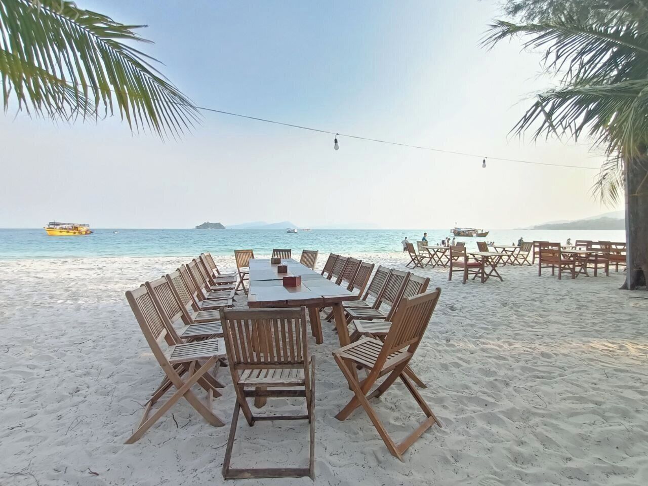 Een eettafel met stoelen aan het strand, omringd door palmbomen met uitzicht op zee.