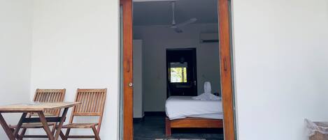 Une piĂšce avec un lit, une porte en bois, un ventilateur de plafond et une fenĂȘtre donnant sur des arbres.