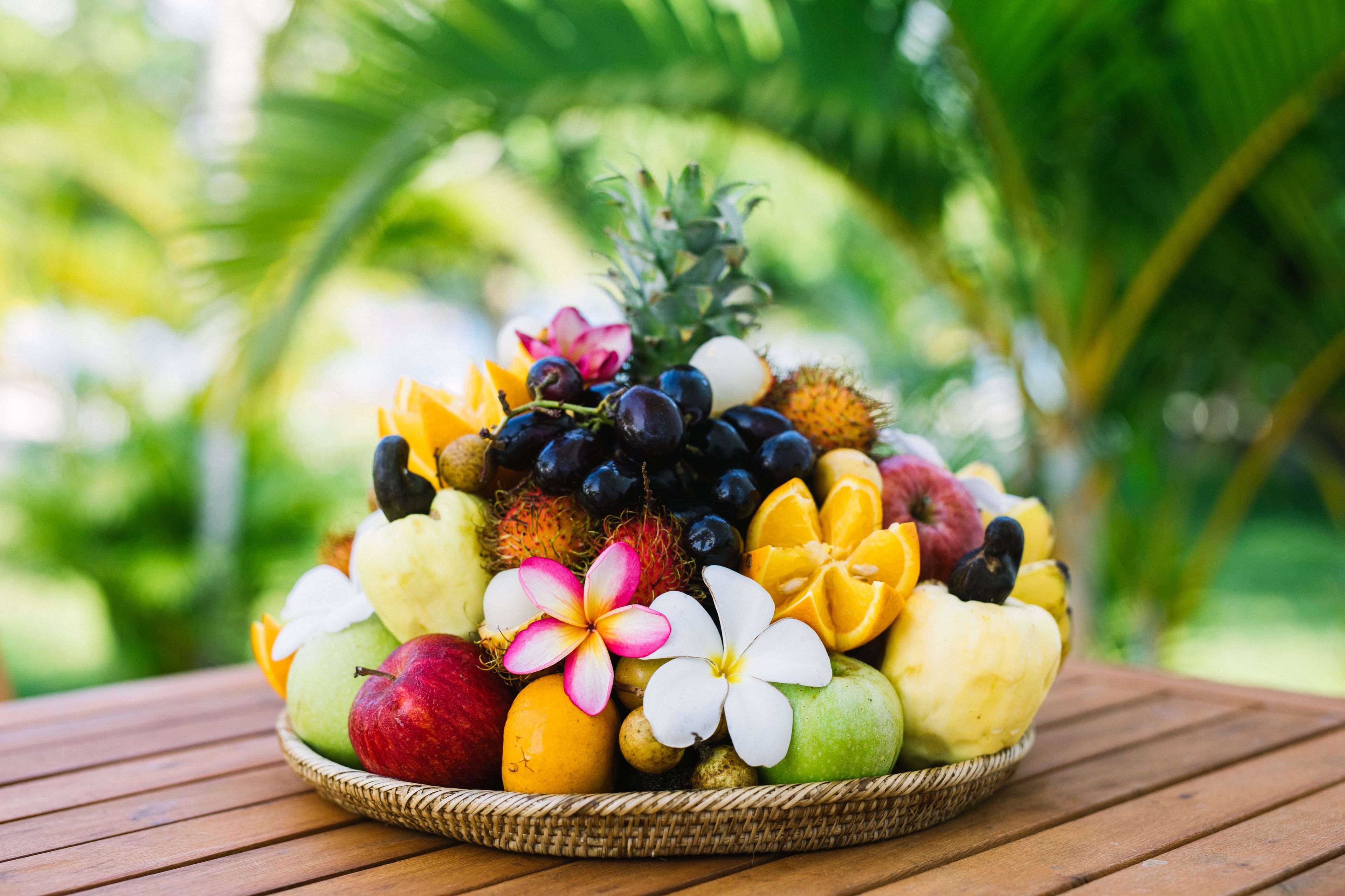 A fruit basket on a wooden table with a blurred green background.