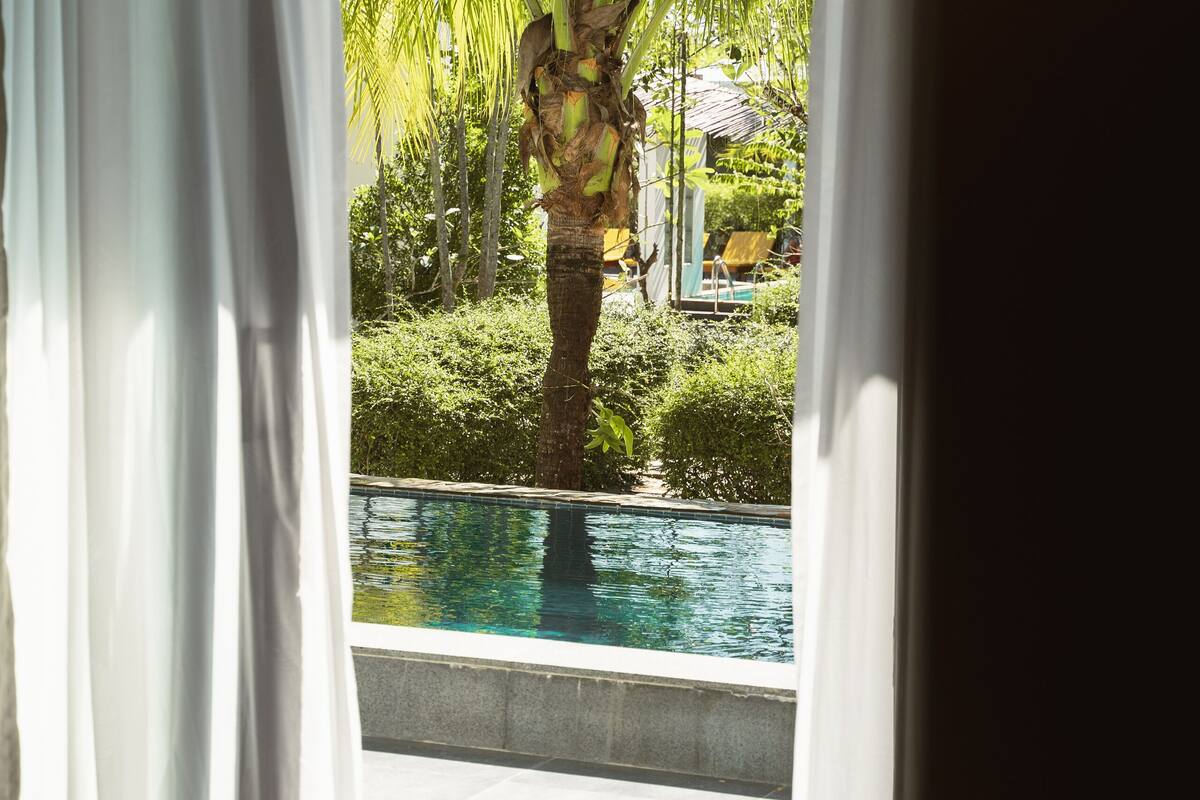 A bedroom with a view of a swimming pool and palm trees.