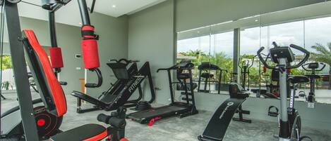 A gym with various exercise equipment, large windows, and a view of greenery outside.