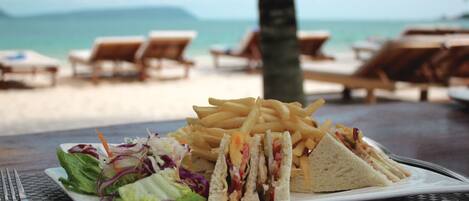 A meal of a sandwich, fries, and salad on a table with a view of the beach and ocean in the background.