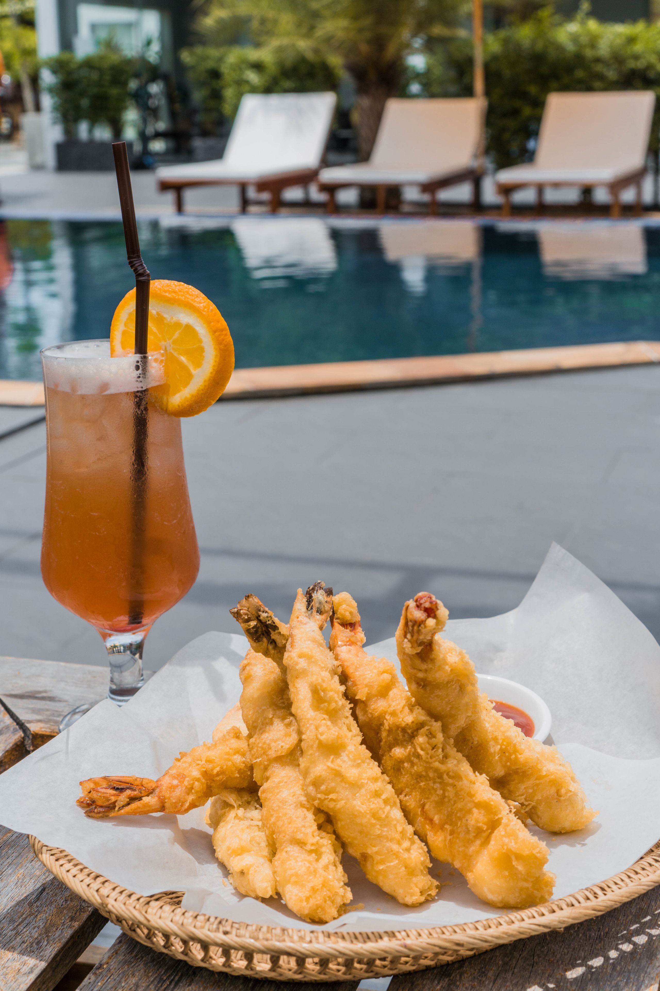 A table with a drink, a basket of fried shrimp, and a poolside setting.
