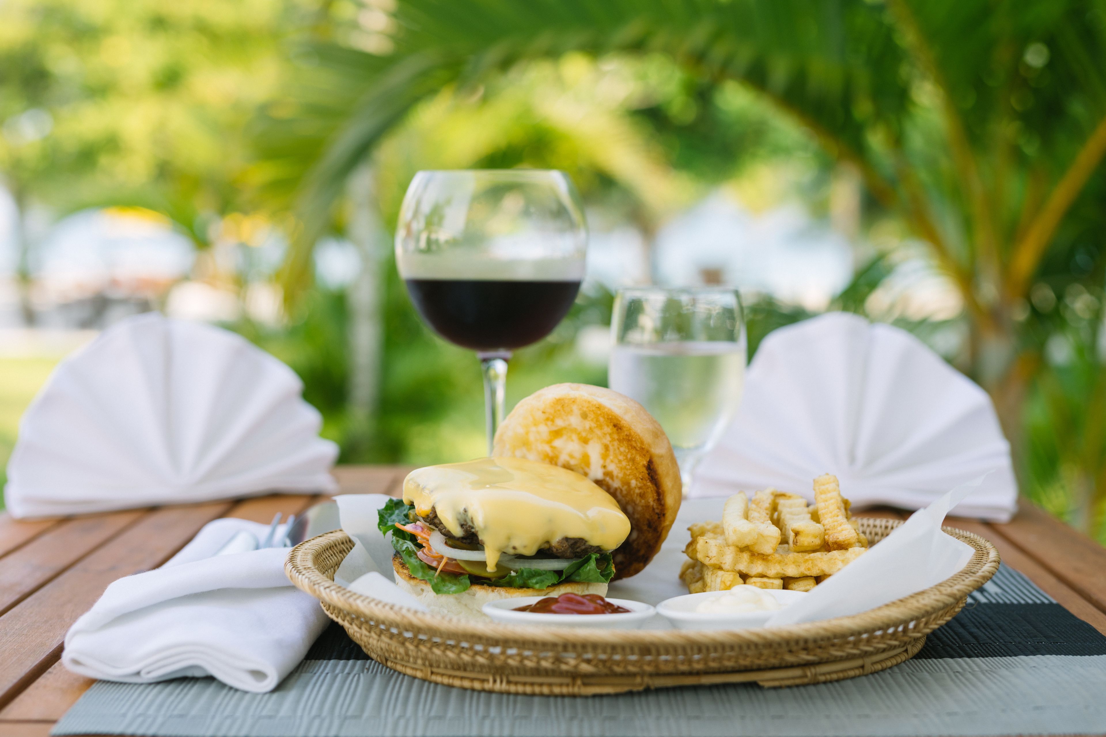 Ein Essen mit einem Burger, Pommes und einem Glas Wein auf einem Holztisch.