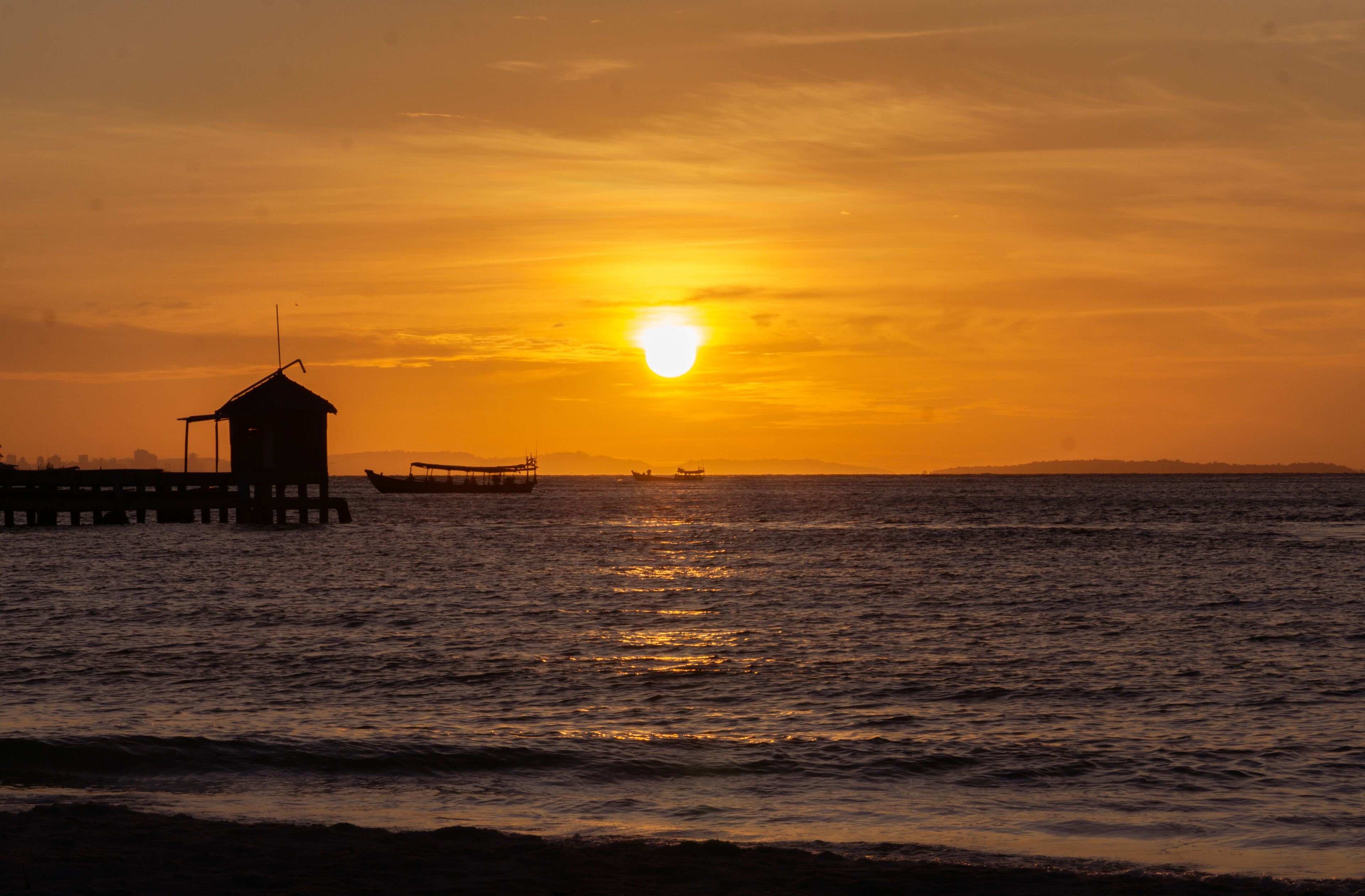 Un atardecer sobre un mar tranquilo con un muelle y barcos.