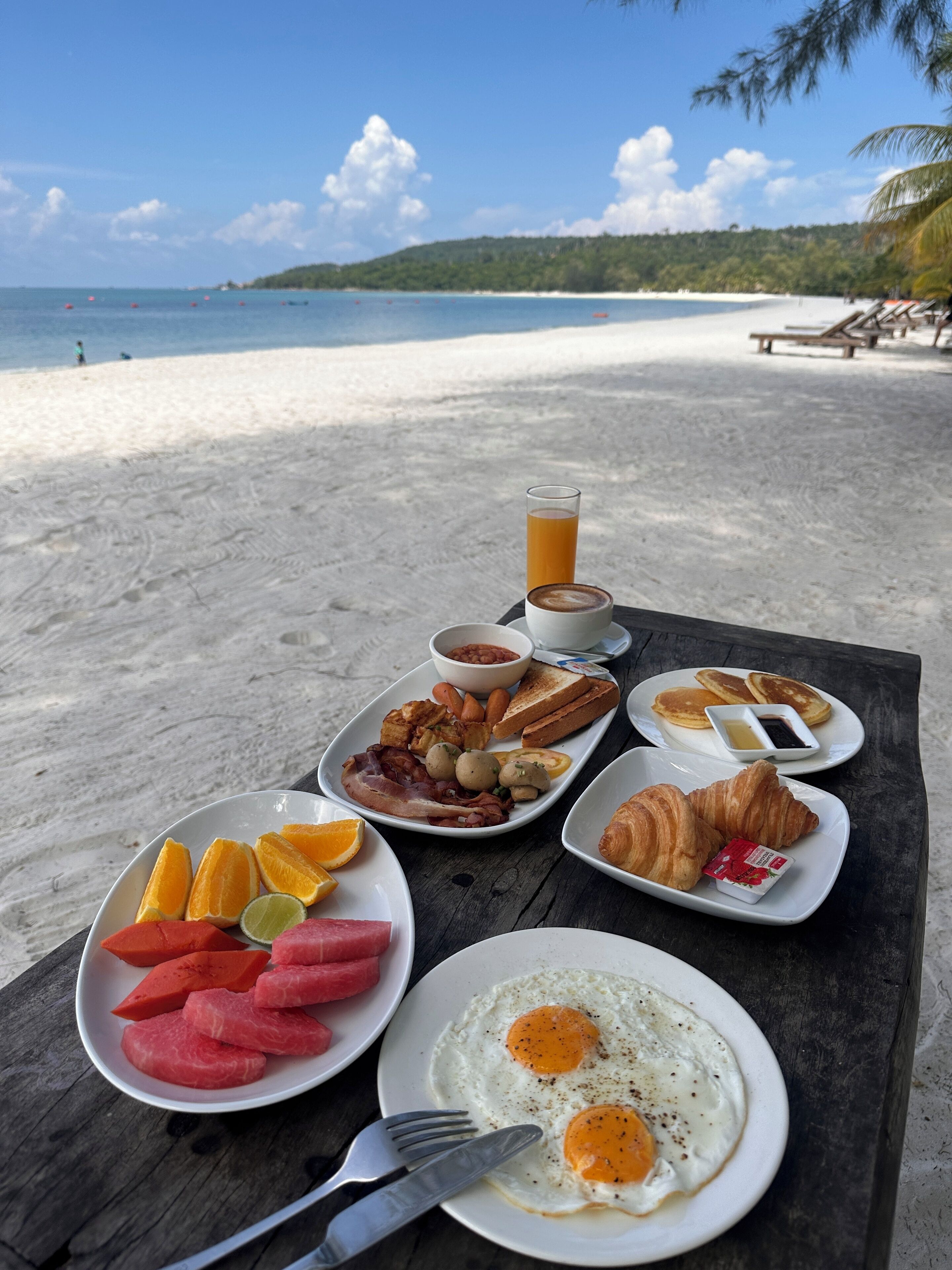 Ein reichhaltiges Frühstücksbuffet auf einem Holztisch mit Blick auf den Strand.