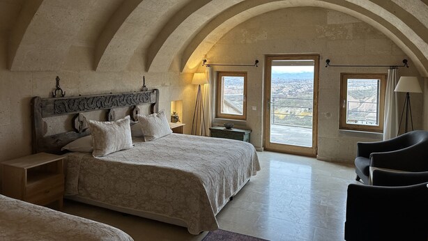 A bedroom with a vaulted ceiling, a large bed, a desk, and two windows offering a view of the landscape. - Kistar Cave Hotel (Nevsehir)