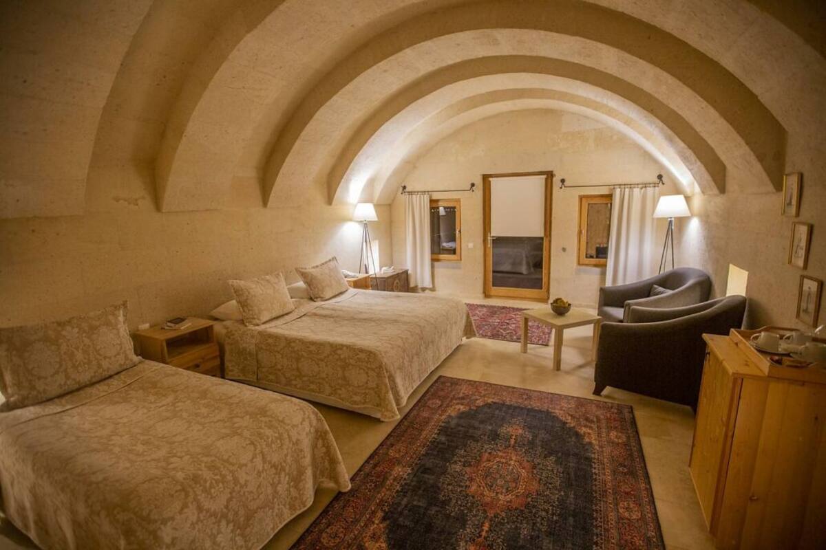 A cozy room with two beds, a sofa, and a small table. The room has an arched ceiling and a fireplace.