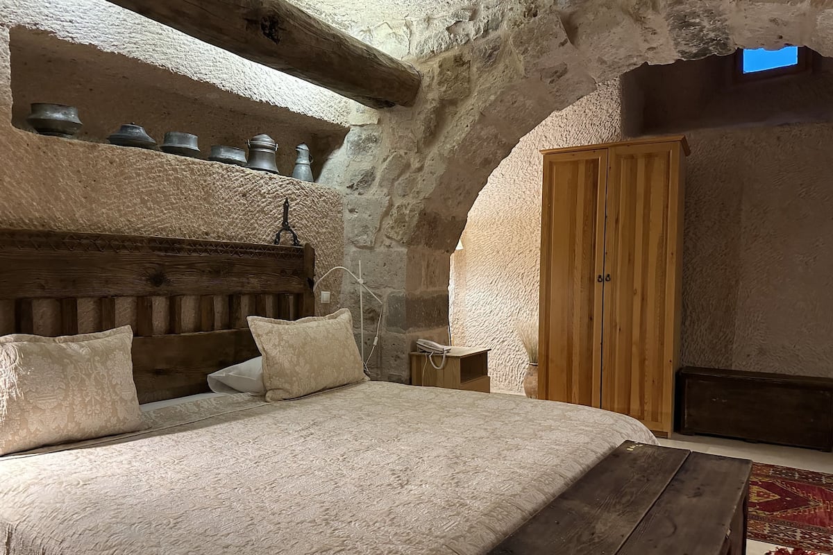 A rustic bedroom with a wooden headboard, a large bed with patterned linens, a wooden bench, and a wooden wardrobe.