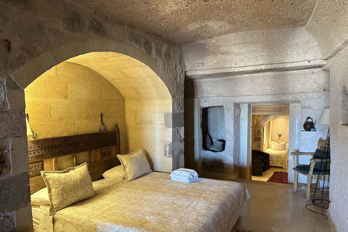 A bedroom with a large arched doorway, a wooden bed with a headboard, a bedside table, and a red rug.