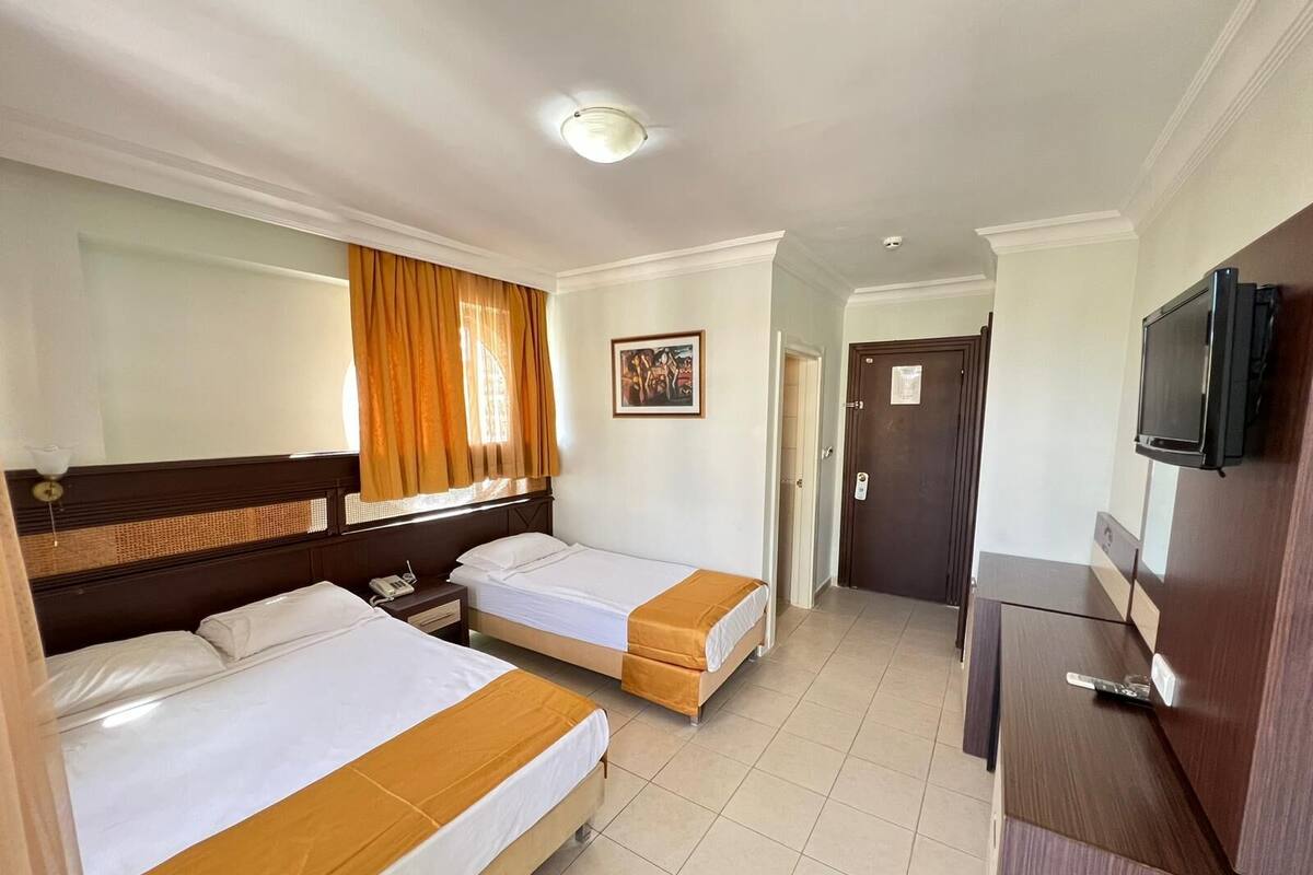 A hotel room with two beds, a desk, a television, and a door leading to a hallway.