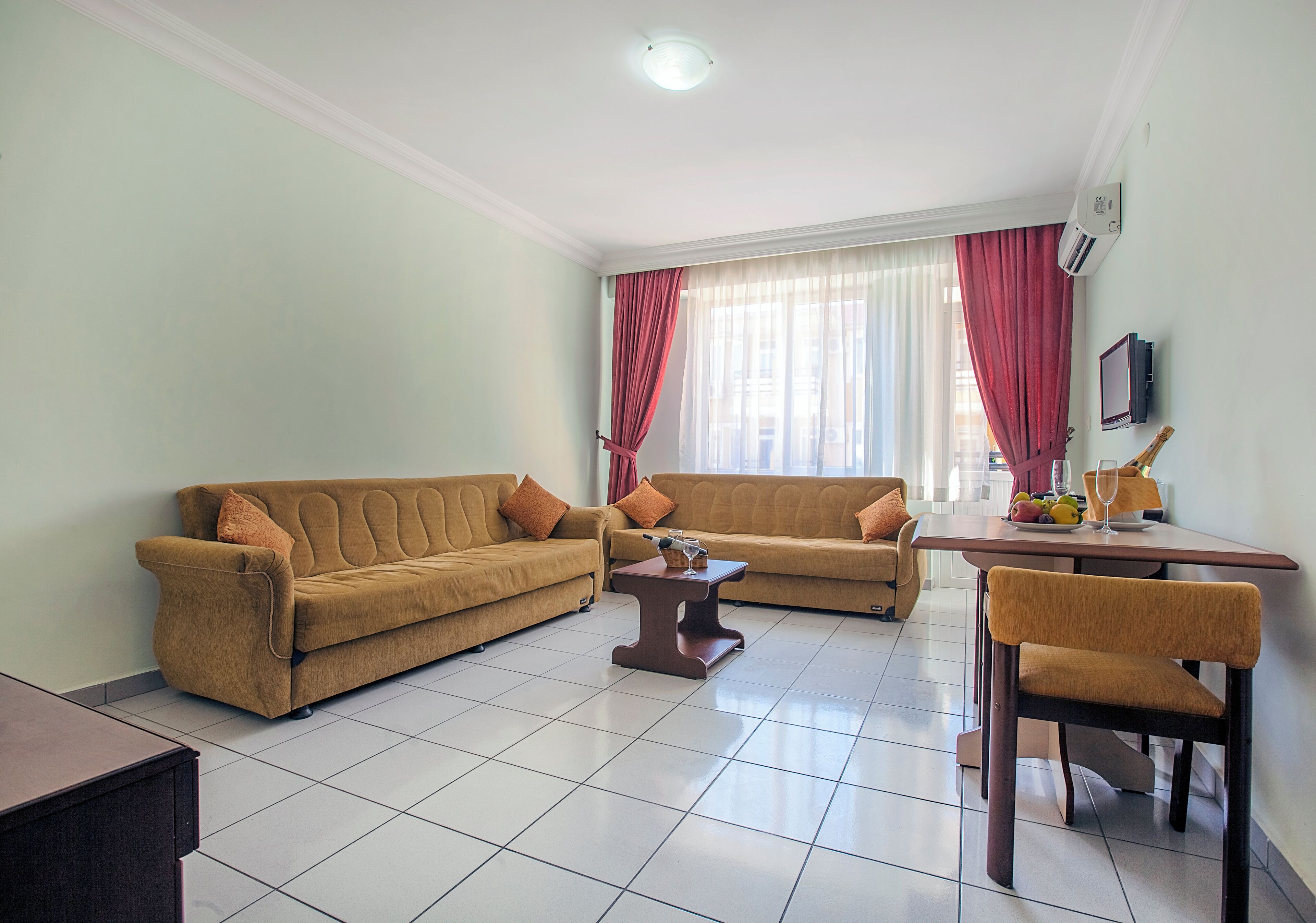 Una sala de estar con dos sofás, una mesa de centro, una mesa de comedor con sillas y un televisor de pantalla plana montado en la pared.