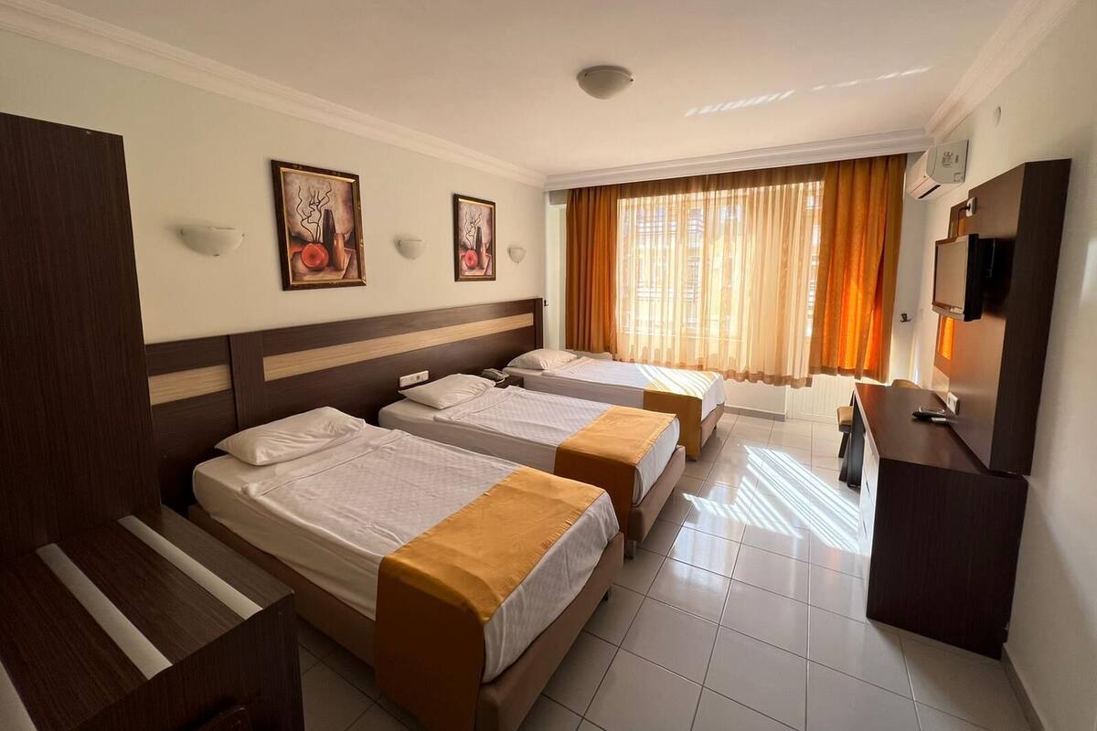A hotel room with two beds, a desk, a TV, and artwork on the wall.