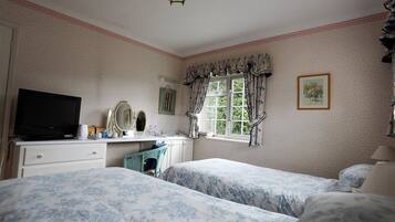 A bedroom with two beds, a dresser, a television, a window with curtains, and a framed picture on the wall.