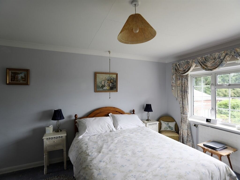 A bedroom with a bed, two nightstands, a hanging lamp, a window with curtains, and a painting on the wall.