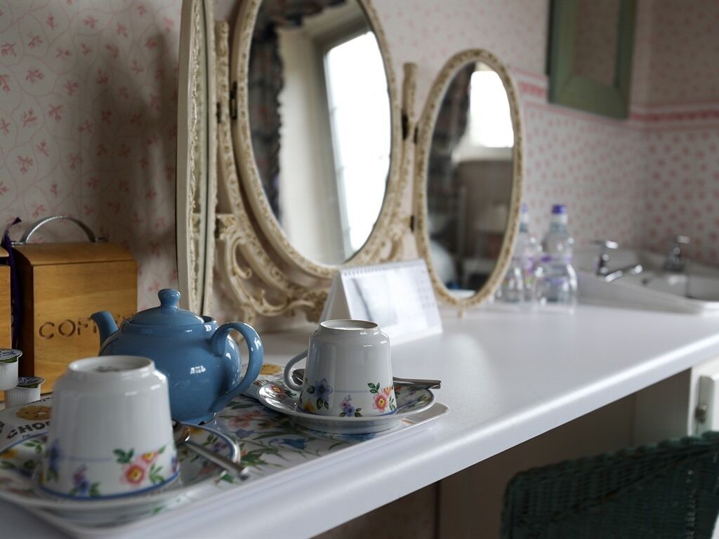 A bathroom with a white sink, a blue teapot, and floral-patterned cups and saucers on a tray.