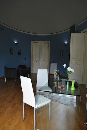 Una sala moderna con una mesa de comedor de vidrio, sillas blancas y una pared azul.