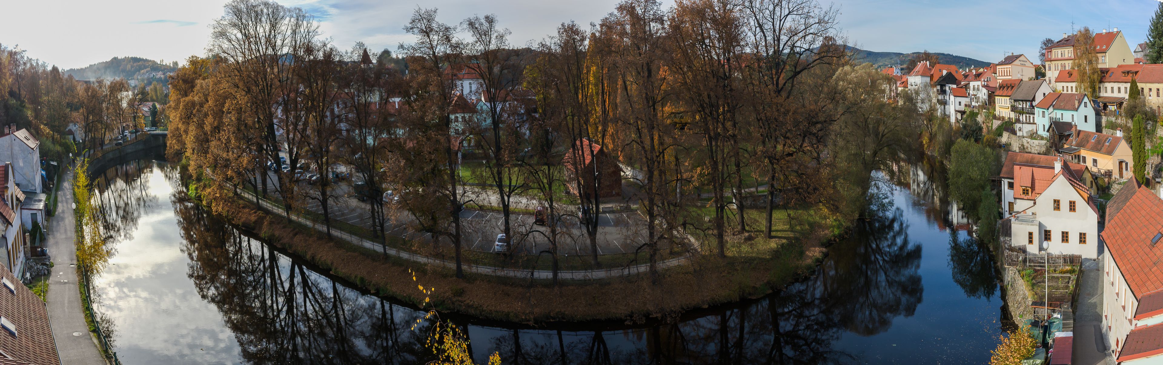 Une vue panoramique d’une ville riveraine, avec ses bâtiments historiques, un pont et un espace vert aménagé en parc.