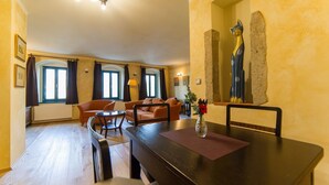 A dining area with a wooden table, chairs, and a vase with flowers. There are two sofas and a small table in the background. - Apartmány U Zvonu (Cesky Krumlov)