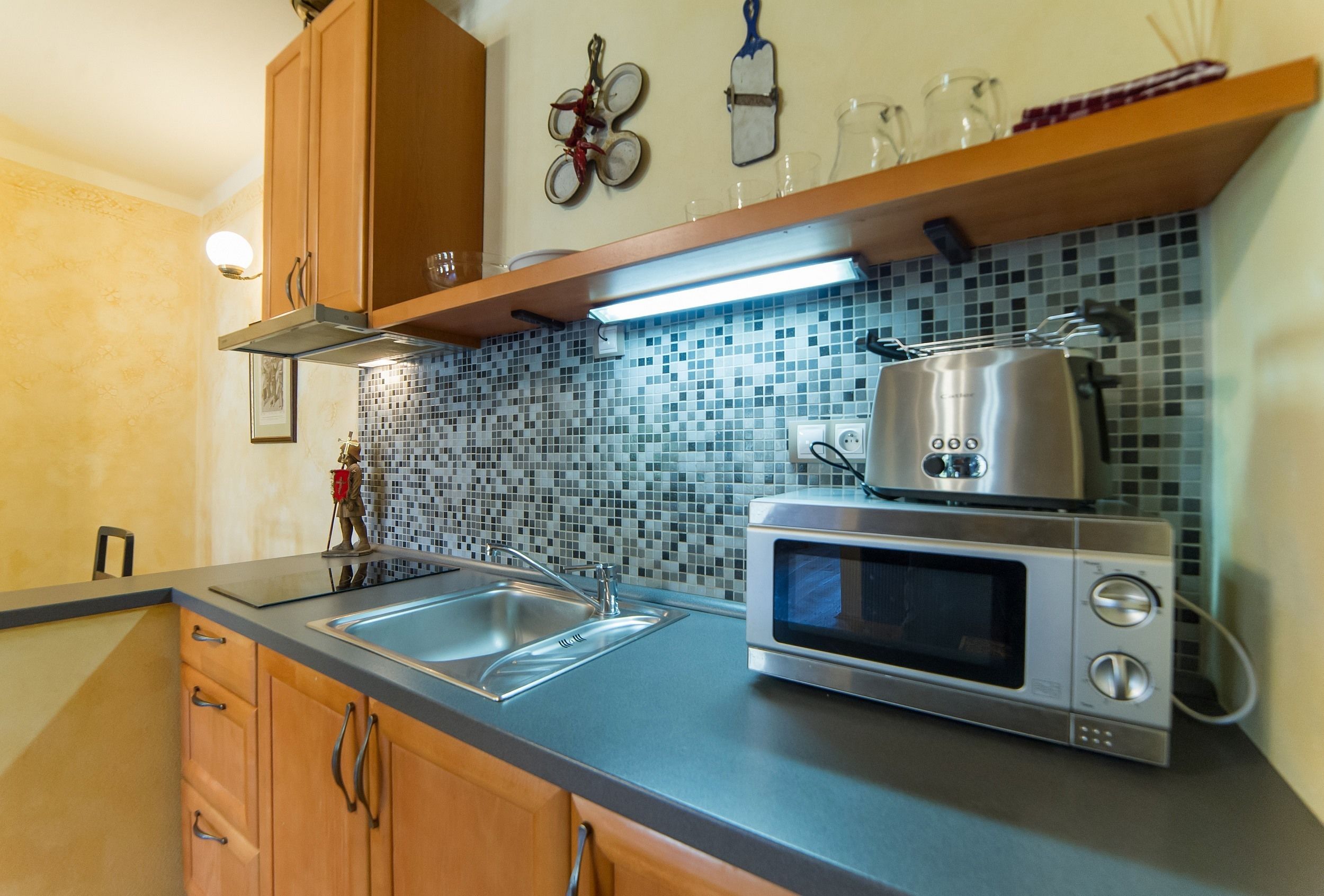 A kitchen with a stainless steel microwave, a sink, wooden cabinets, and a tiled backsplash.