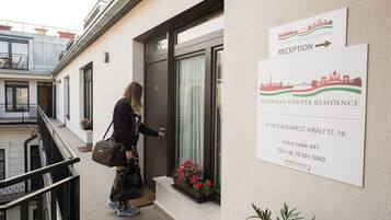 Een vrouw die een gebouw binnenstapt, met een bord voor de receptie en een bord van Budapest Center Residence.