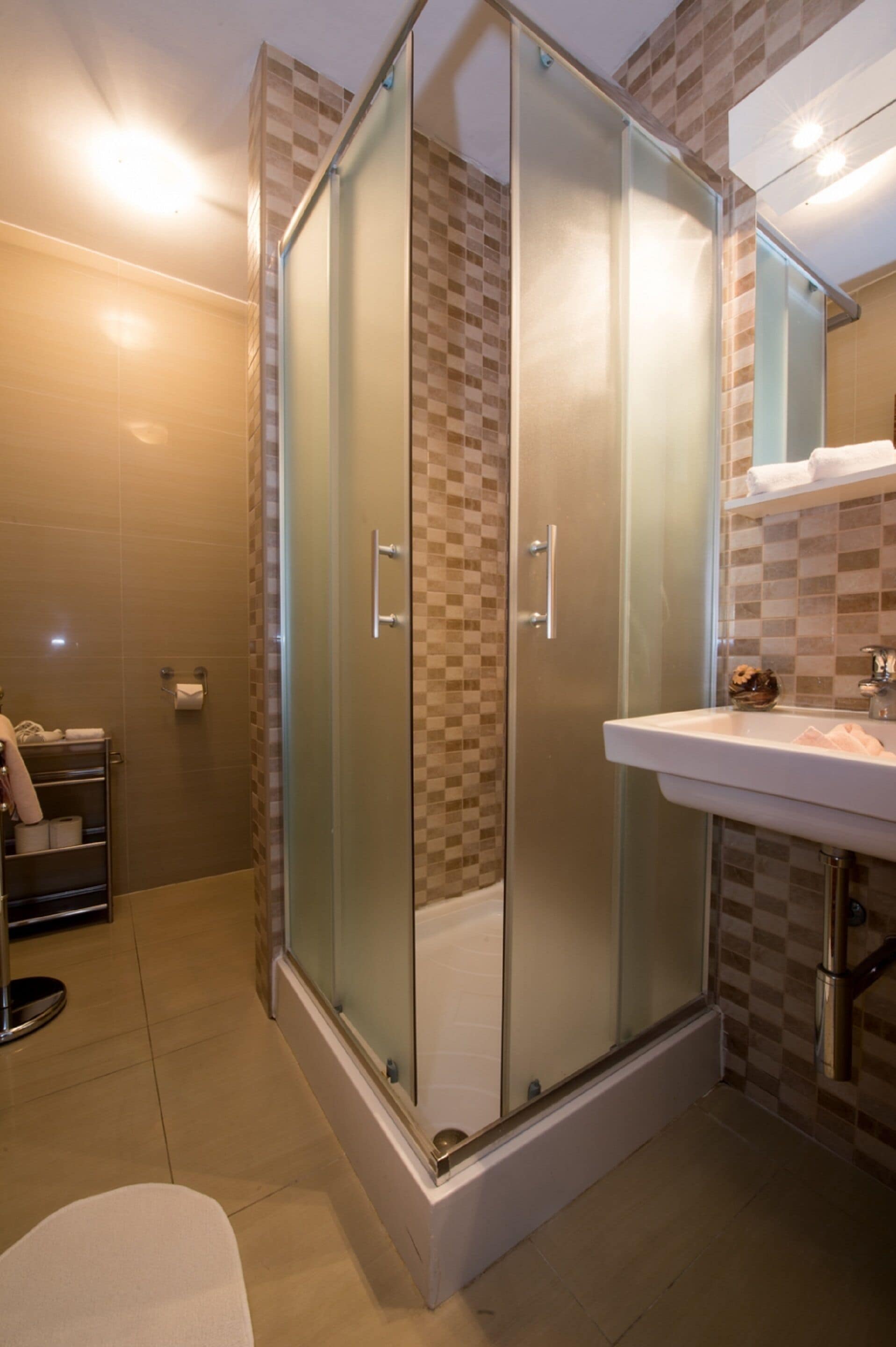 A modern bathroom with a glass-enclosed shower, a white sink, and a tiled wall.