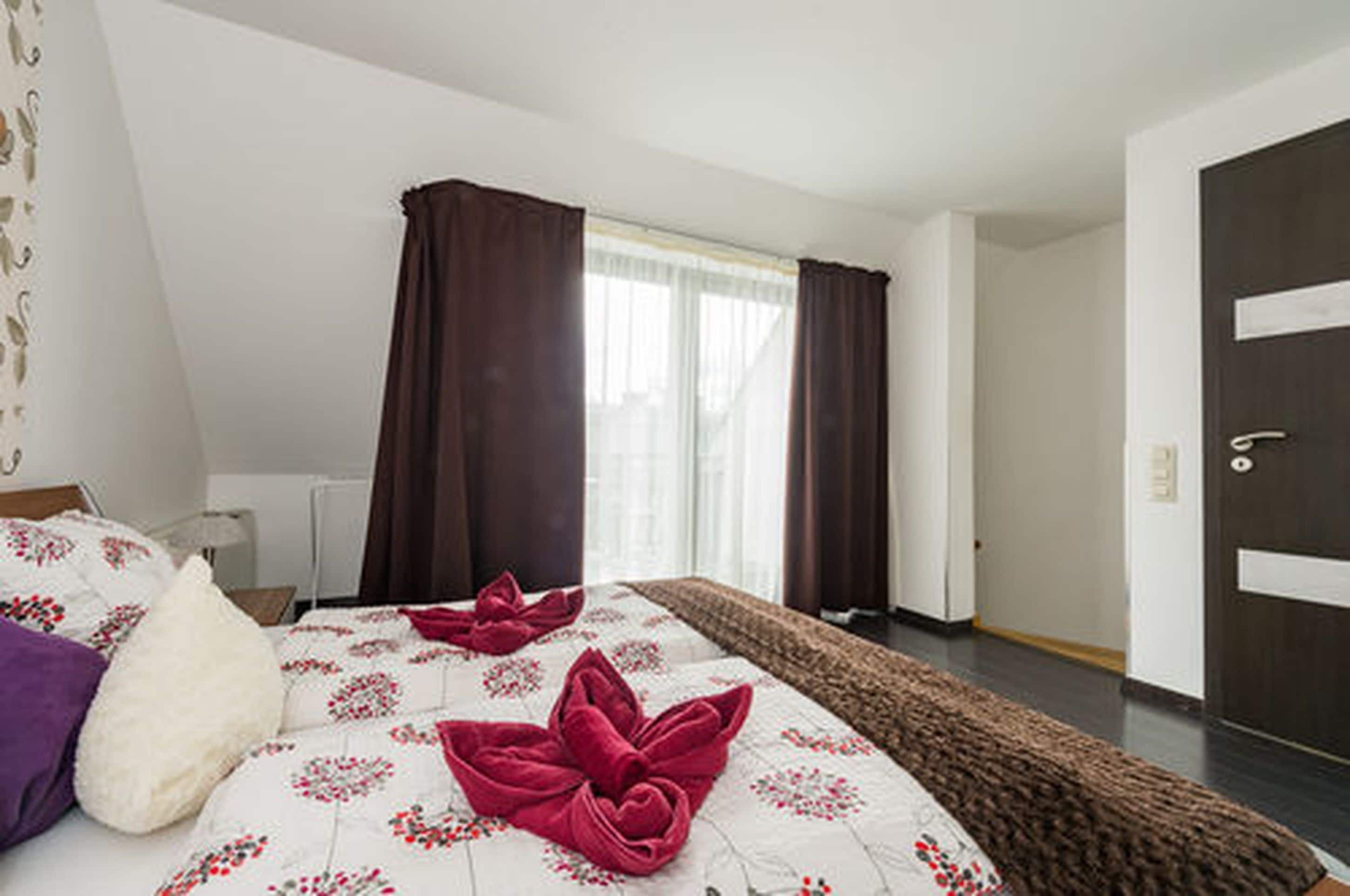 Hotellihuone, jossa on sänky, ikkuna verhoineen, ovi ja yöpöytä.