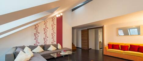 A modern living room with a gray sectional sofa, a yellow sofa with red cushions, a glass coffee table, and a patterned rug.