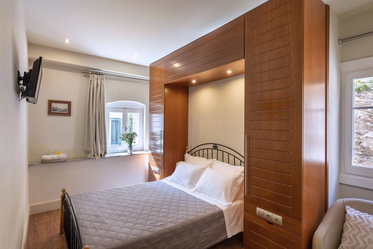 A bedroom with a bed, wooden paneling, a window, and a mounted television.