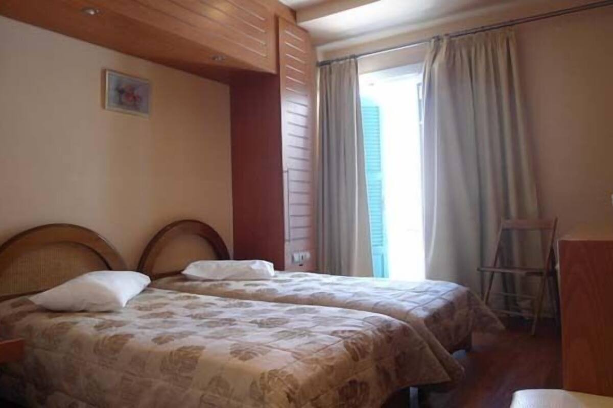 A bedroom with two beds, wooden headboards, a wooden dresser, and a window with curtains.