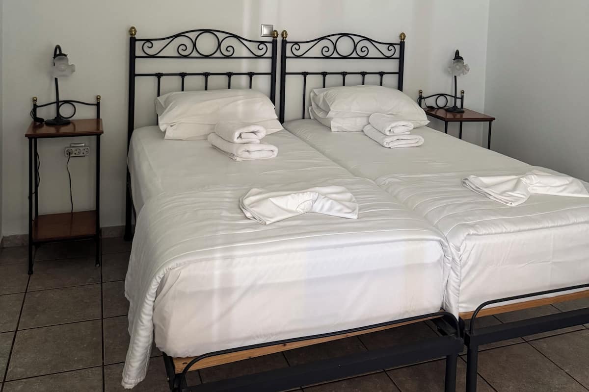 Cama doble con ropa blanca, dos mesitas de noche con lámparas y un equipo de aire acondicionado en la pared.