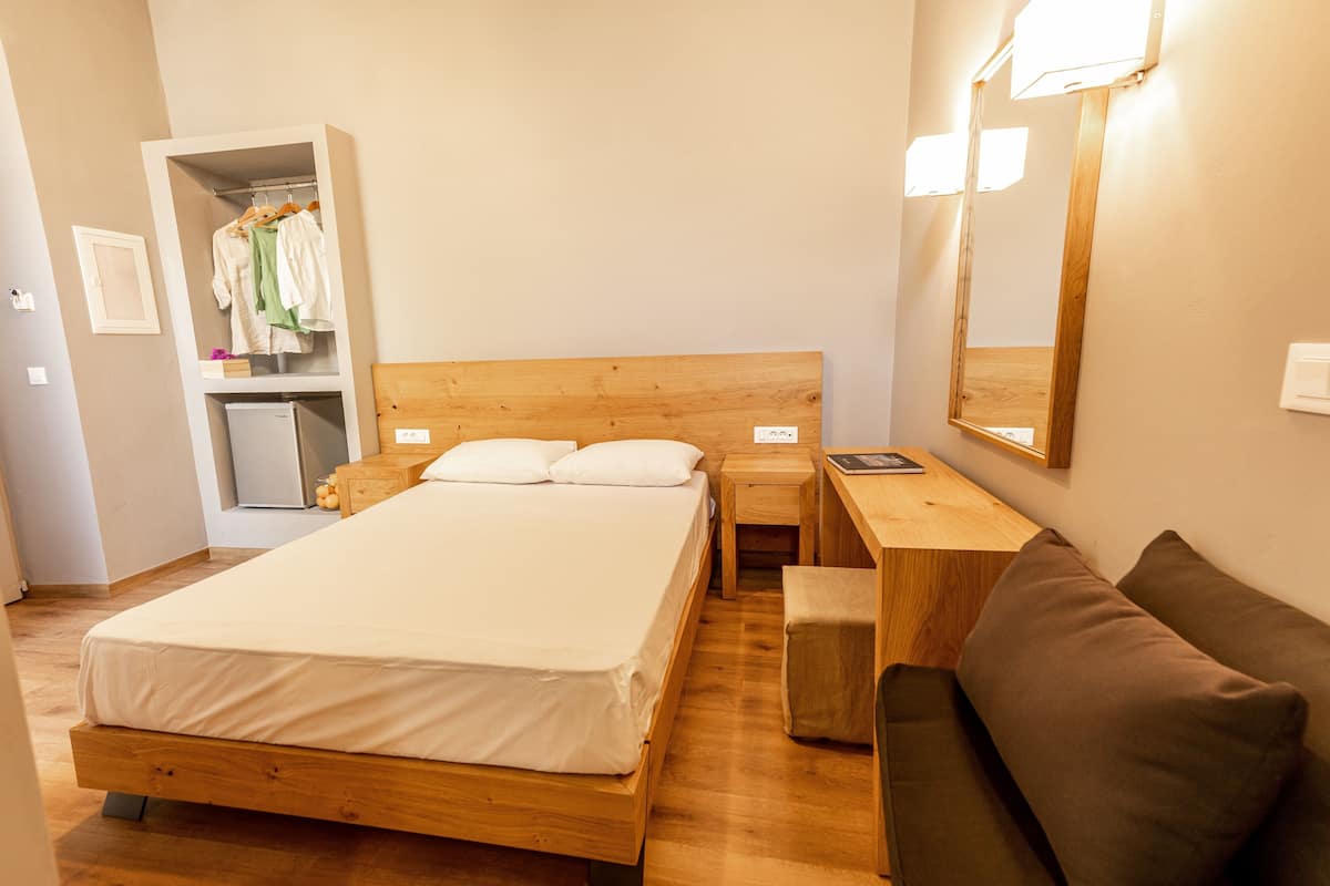 Un dormitorio con una cama de madera, una mesita de noche, un escritorio pequeño, un banco, un armario y un espejo.