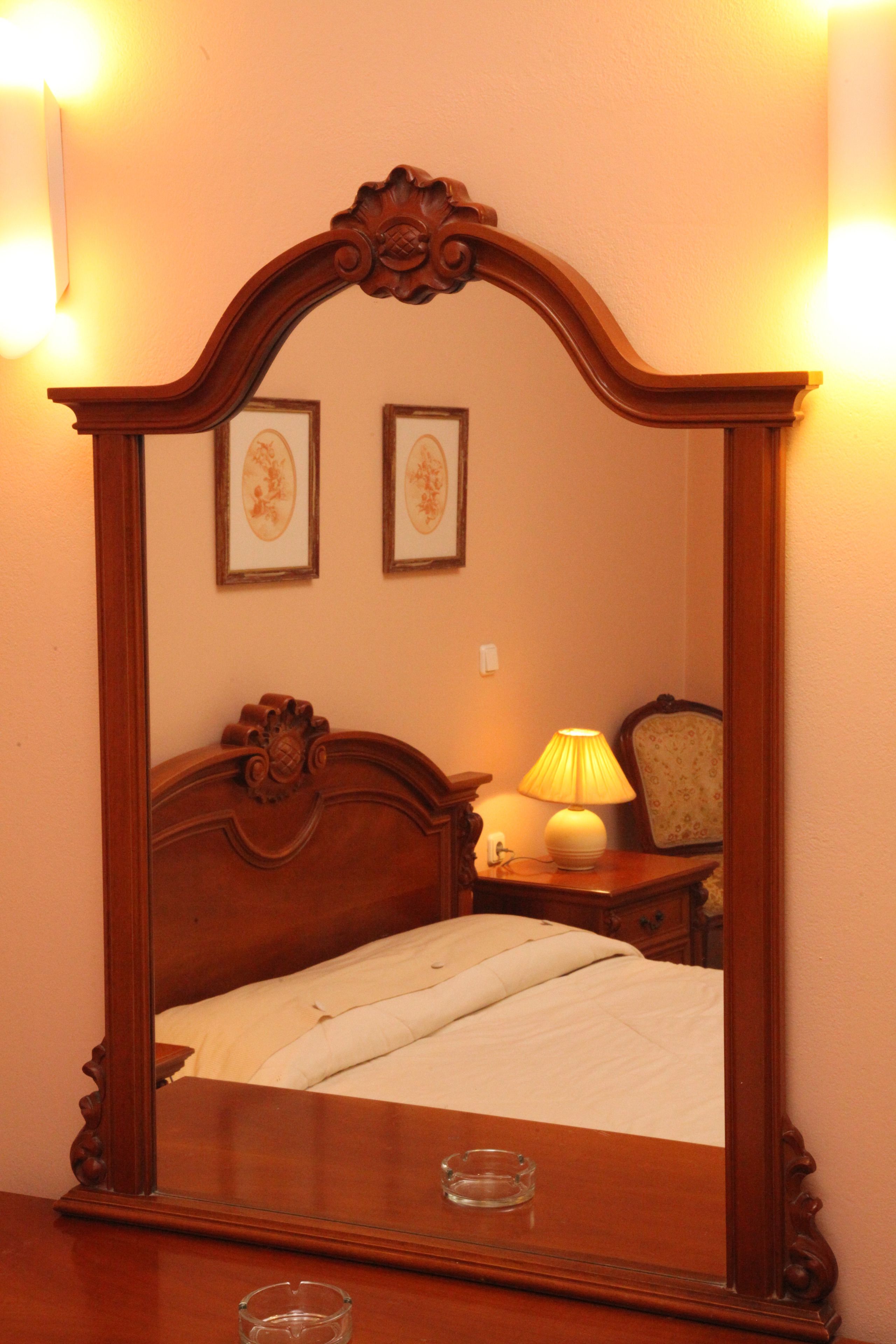 Ein Schlafzimmer mit Holz-Kopfteil, einer Nachttischlampe, einem gerahmten Bild an der Wand und einem Nachttischchen mit einem Glas.