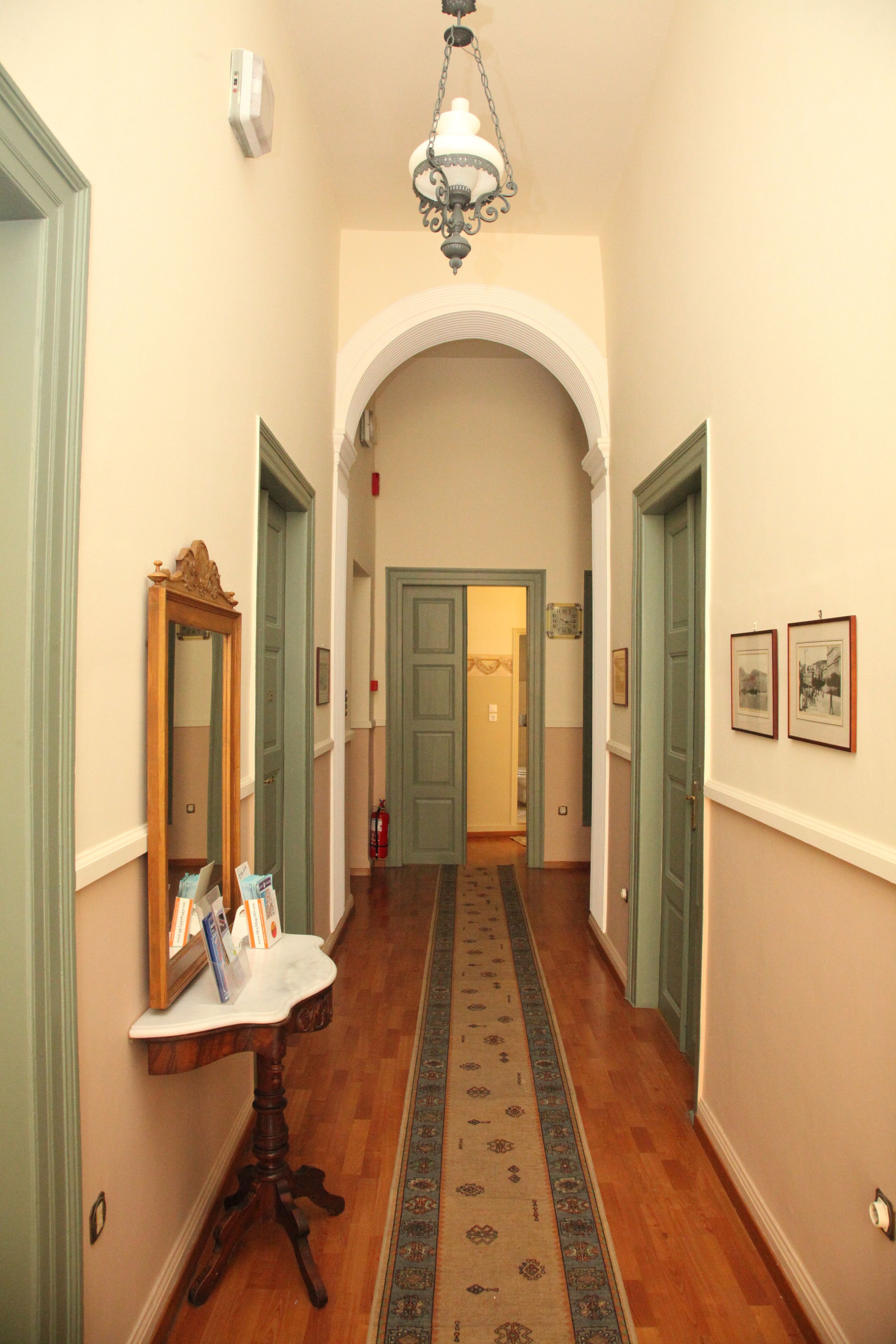 A hallway with a wooden floor, a white table with a mirror and books, and a chandelier.