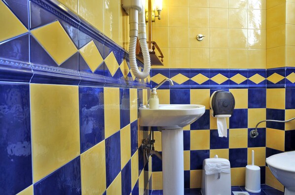 Un baño con baldosas de cuadros amarillos y azules, un lavamanos blanco, un inodoro y un dispensador de toallas de papel.