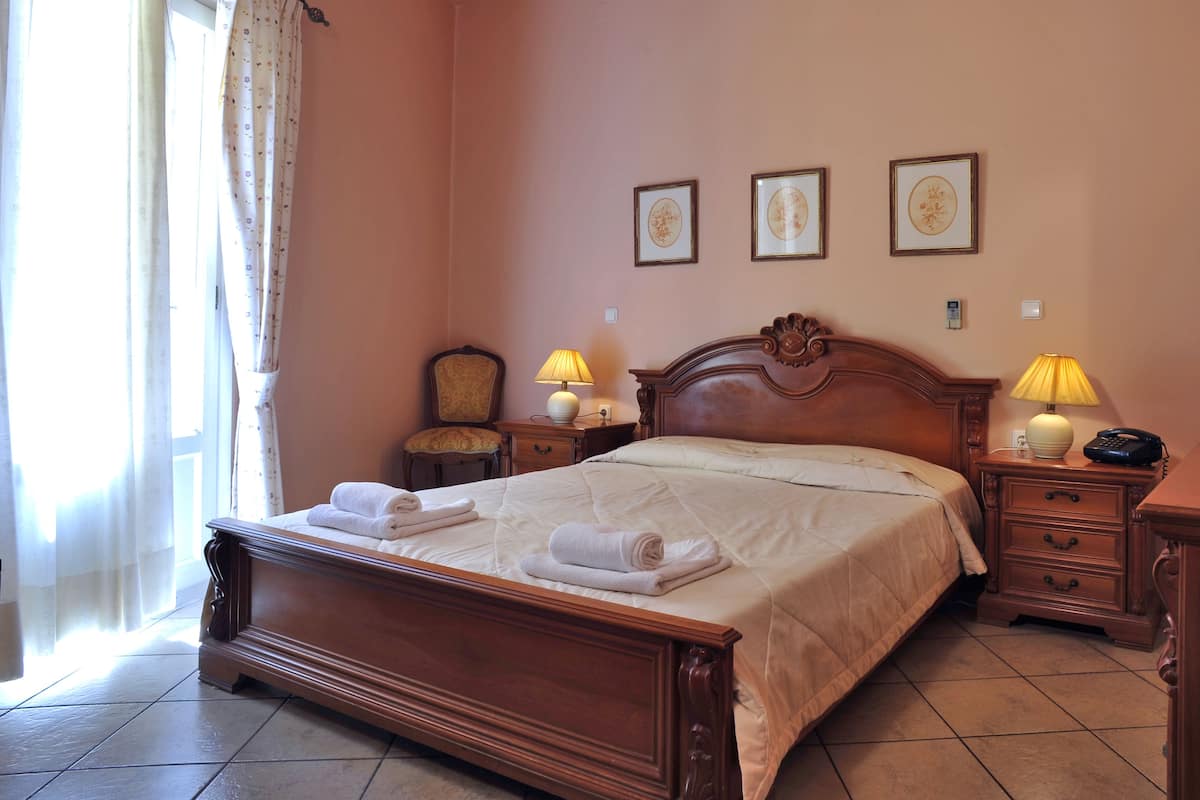 Una cama bien hecha con toallas, un cabecero de madera, lámparas de noche, una silla y cuadros en la pared.