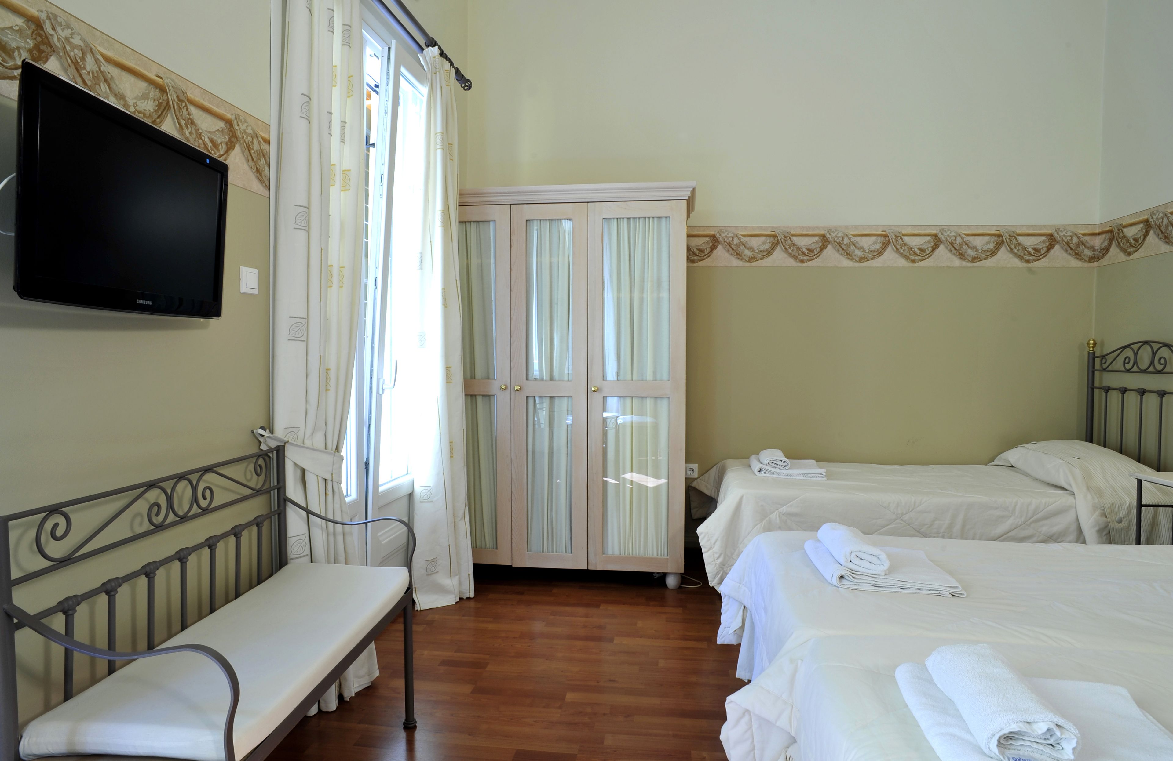 A hotel room with a bed, a bench, a TV, and a wardrobe.