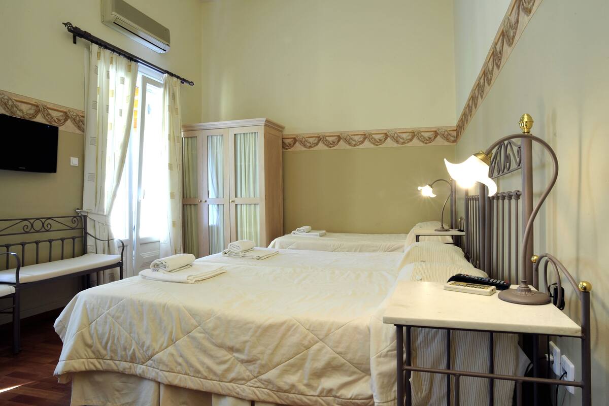 Habitación de hotel con dos camas, un escritorio, una silla, un televisor y una ventana con cortinas.