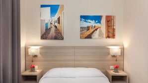 Een hotelkamer met een bed, twee nachtkastjes met lampen, en twee wanddecoraties van straten.