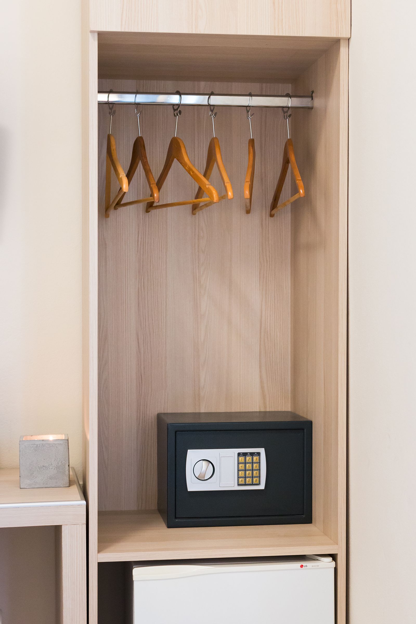 A wooden wardrobe with a black safe, a small table with a block, and wooden hangers on a rod.