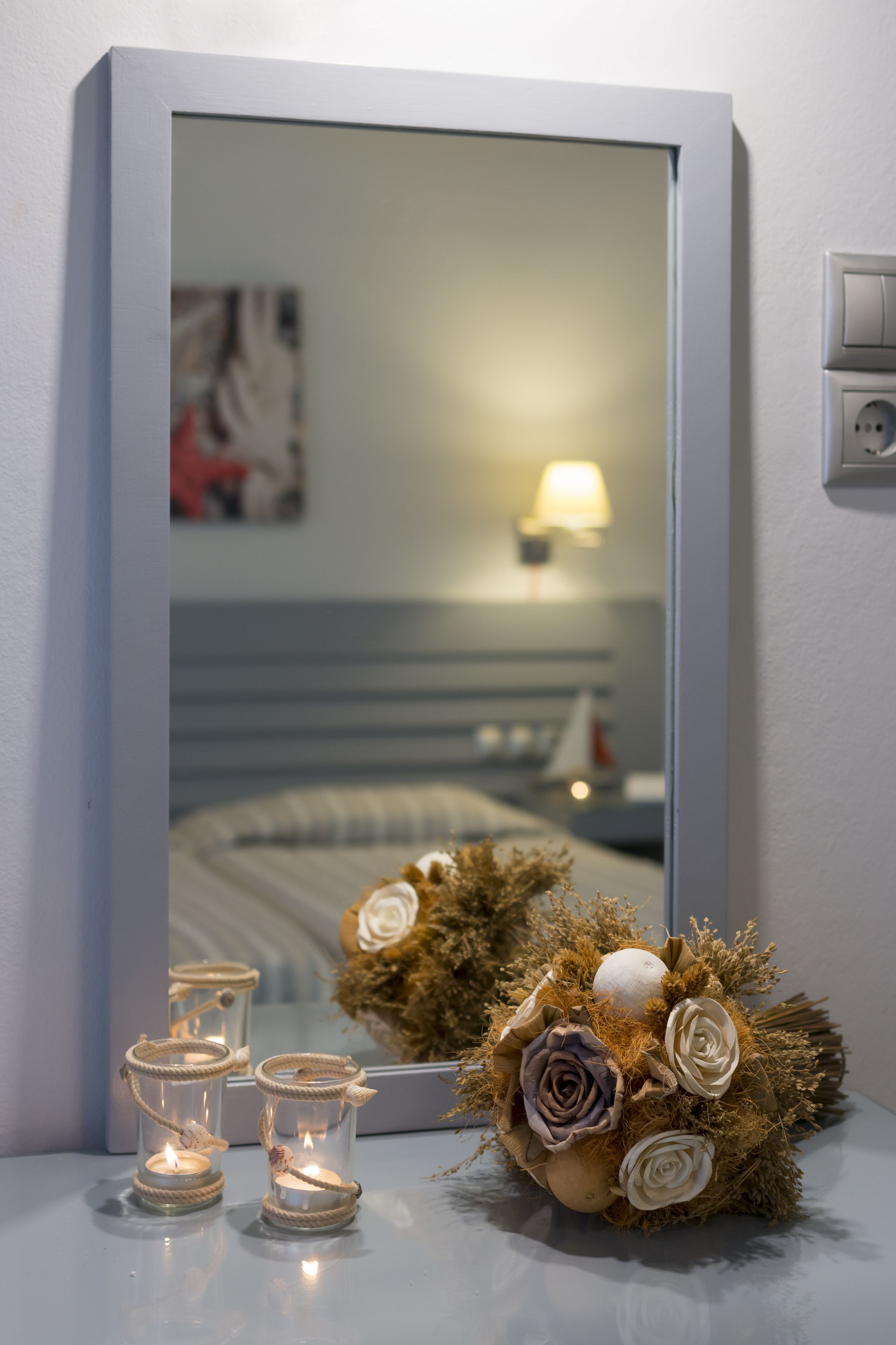 Un miroir reflétant un lit, une lampe et une composition décorative agrémentée de bougies et de fleurs.